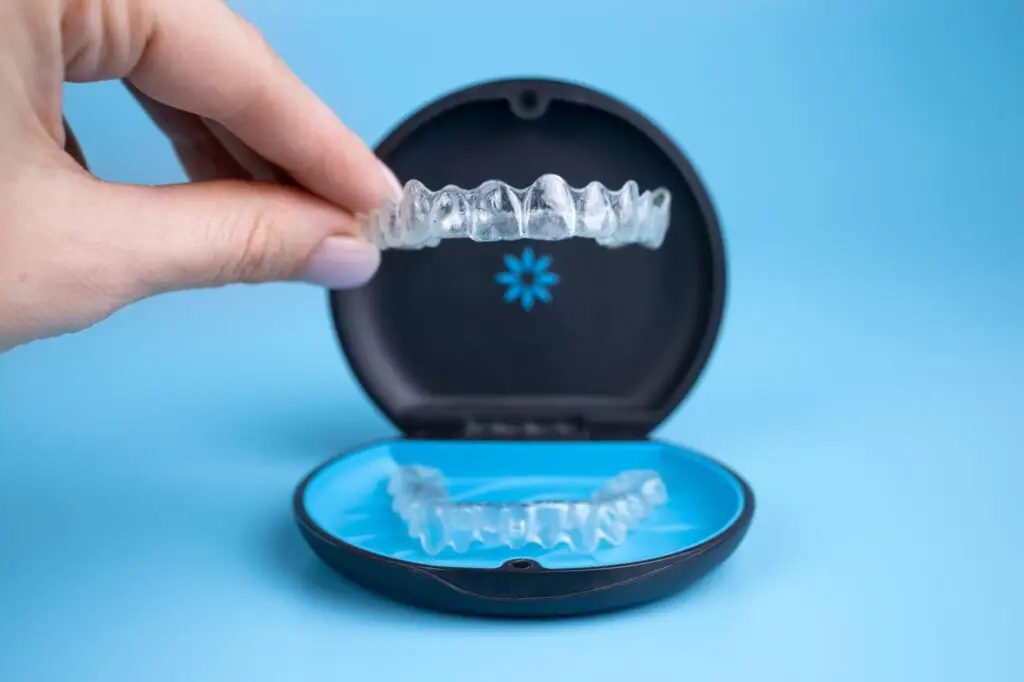 Hand holding Invisalign clear aligner above case — nearly invisible and removable for discreet orthodontic treatment.