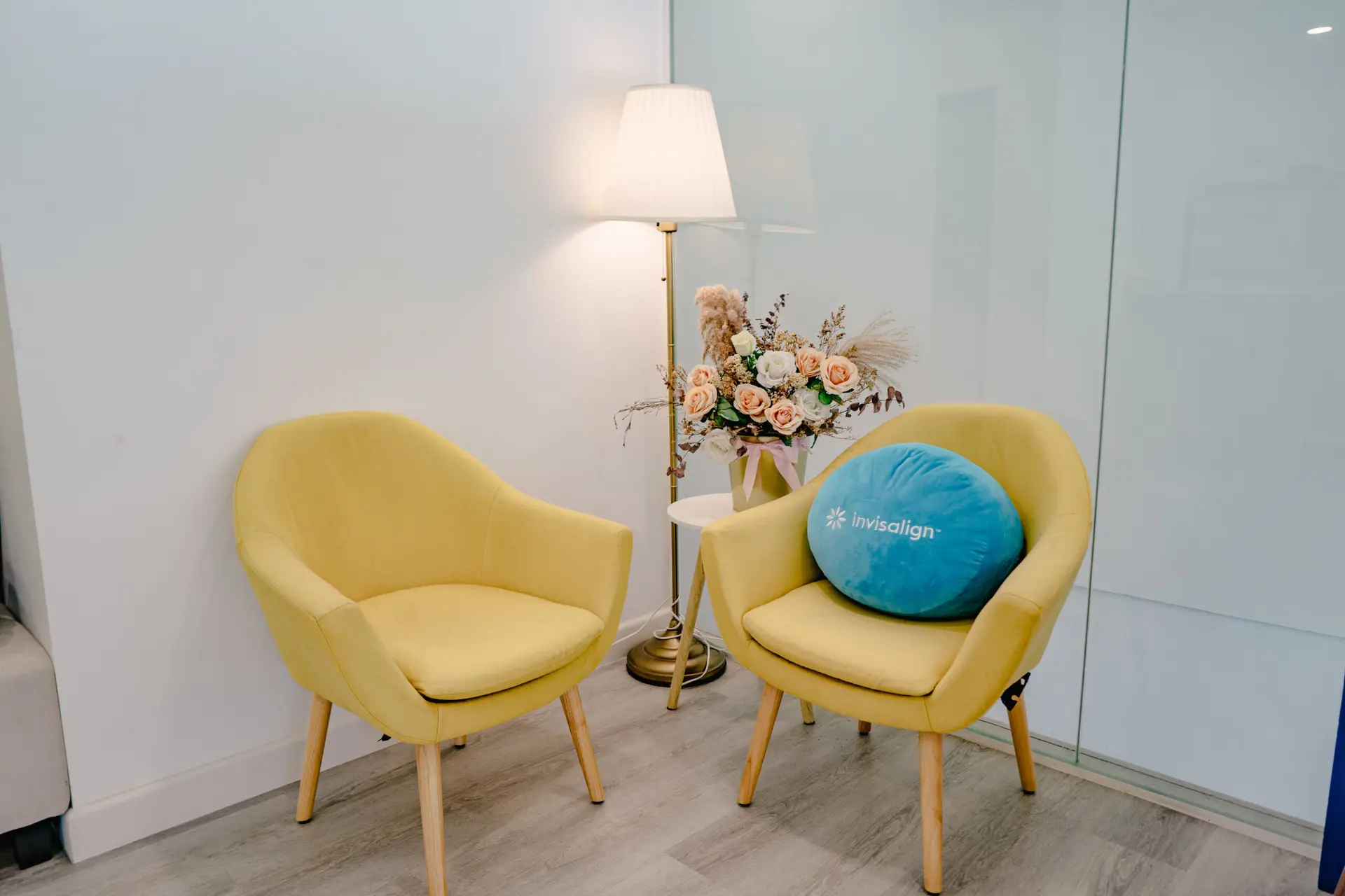 Minimalist consultation corner at Oralis Dental featuring yellow chairs, floral decor, and an Invisalign-branded pillow.
