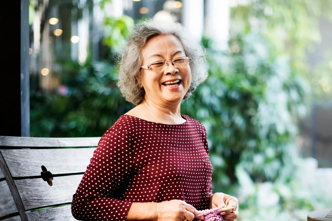 Smiling elderly woman sitting on a bench in a park, showcasing her healthy teeth and bright smile. The image highlights the importance of long-term oral health and restorative dentistry, emphasizing services from a Dental Clinic in Petaling Jaya.
