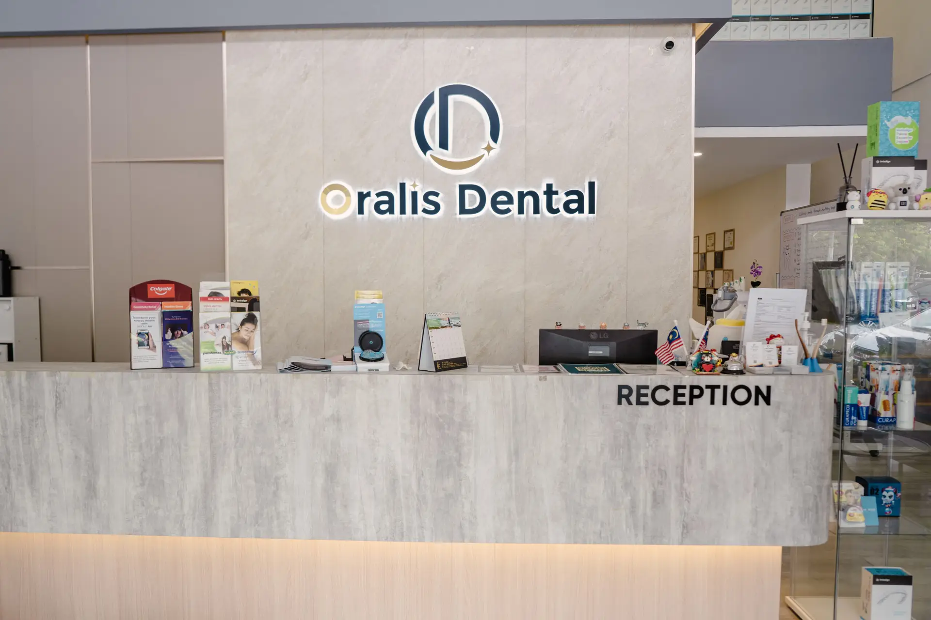 Branded reception desk at Oralis Dental Petaling Jaya with Malaysian and US flags, brochures, and a glass display of dental products.