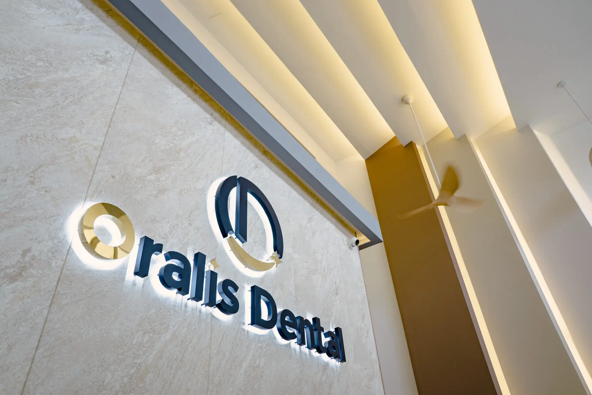 Illuminated Oralis Dental logo on a marble-textured wall in Petaling Jaya, showcasing modern clinic branding.